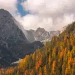 Escursionista su sentiero di montagna in autunno con vista sulle cime dolomitiche e boschi dorati