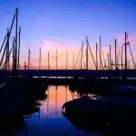 Bicchieri di vino tinto e spritz che si incontrano al tramonto su una terrazza con vista sul mare e barche ormeggiate