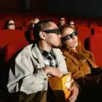 Pubblico seduto in sala cinematografica durante una proiezione, con schermi digitali sullo sfondo