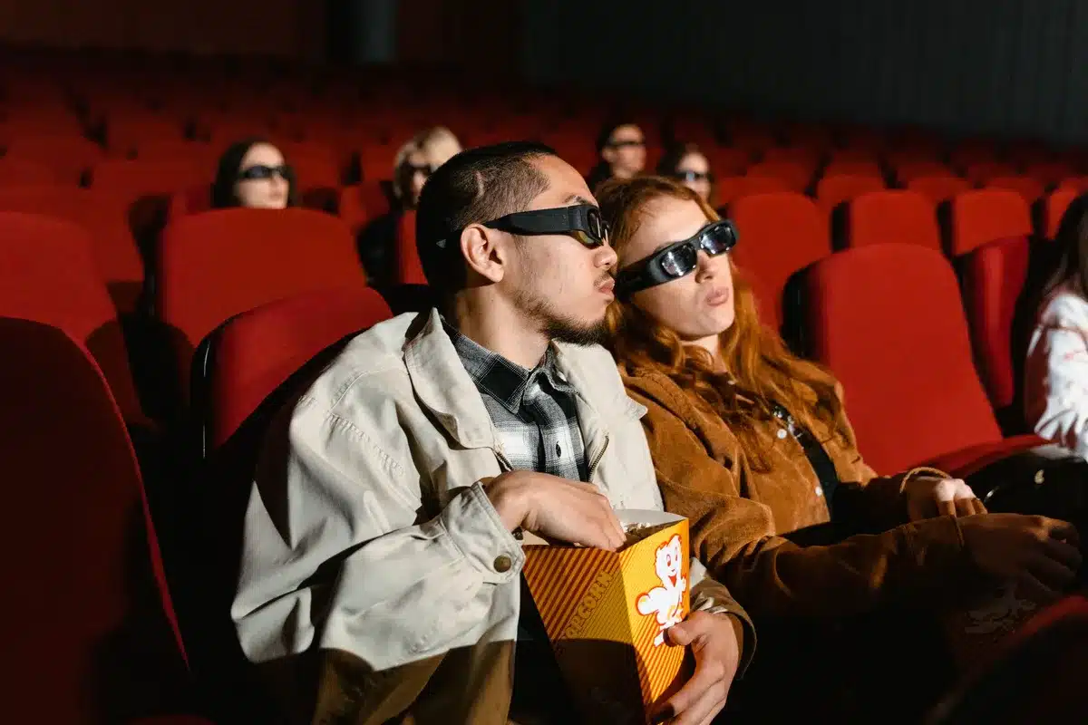 Pubblico seduto in sala cinematografica durante una proiezione, con schermi digitali sullo sfondo