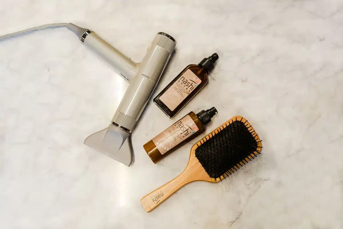 Flaconi di prodotti per capelli leggeri: siero e leave-in su superficie bianca