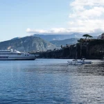 Folla di turisti anonimi su una banchina costiera con barche e scogliere sullo sfondo