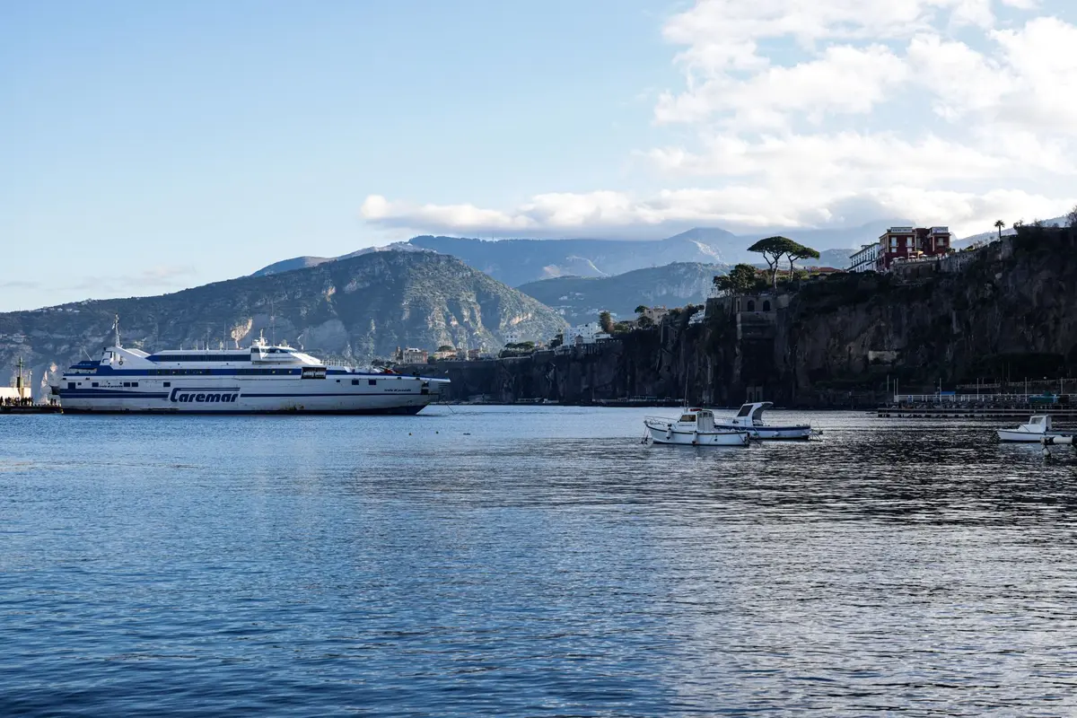 Folla di turisti anonimi su una banchina costiera con barche e scogliere sullo sfondo