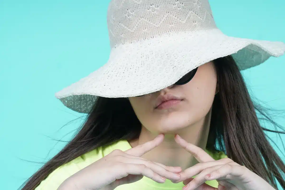 Persona con cappello a tesa larga che applica protezione solare al cuoio capelluto in ambiente esterno soleggiato