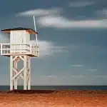 Spiaggia affollata al tramonto con strutture balneari illuminate e figure di persone in lontananza