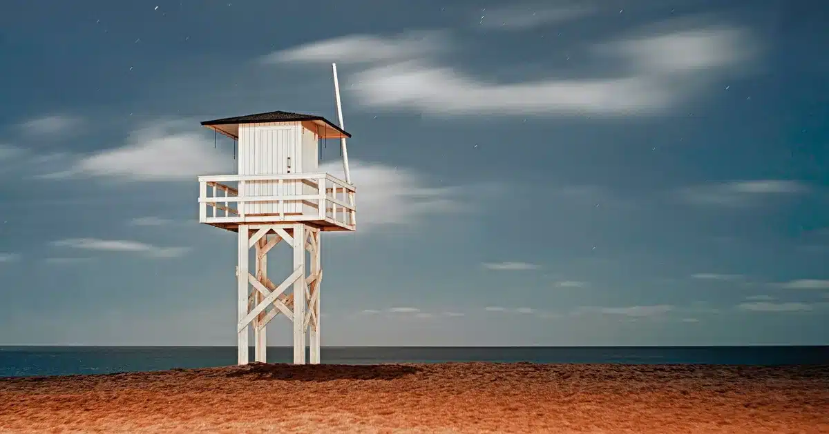 Spiaggia affollata al tramonto con strutture balneari illuminate e figure di persone in lontananza