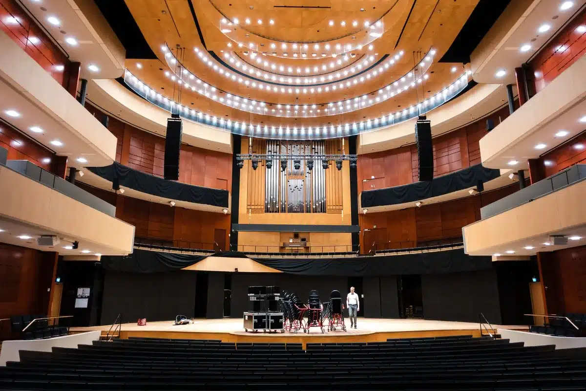 Interno di un teatro storico con platea, palco illuminato e sedute rosse, pronto per un grande evento.