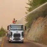 Vigili del fuoco con cannoni ad acqua aerei combattono un incendio boschivo su un pendio con fiamme e fumo denso
