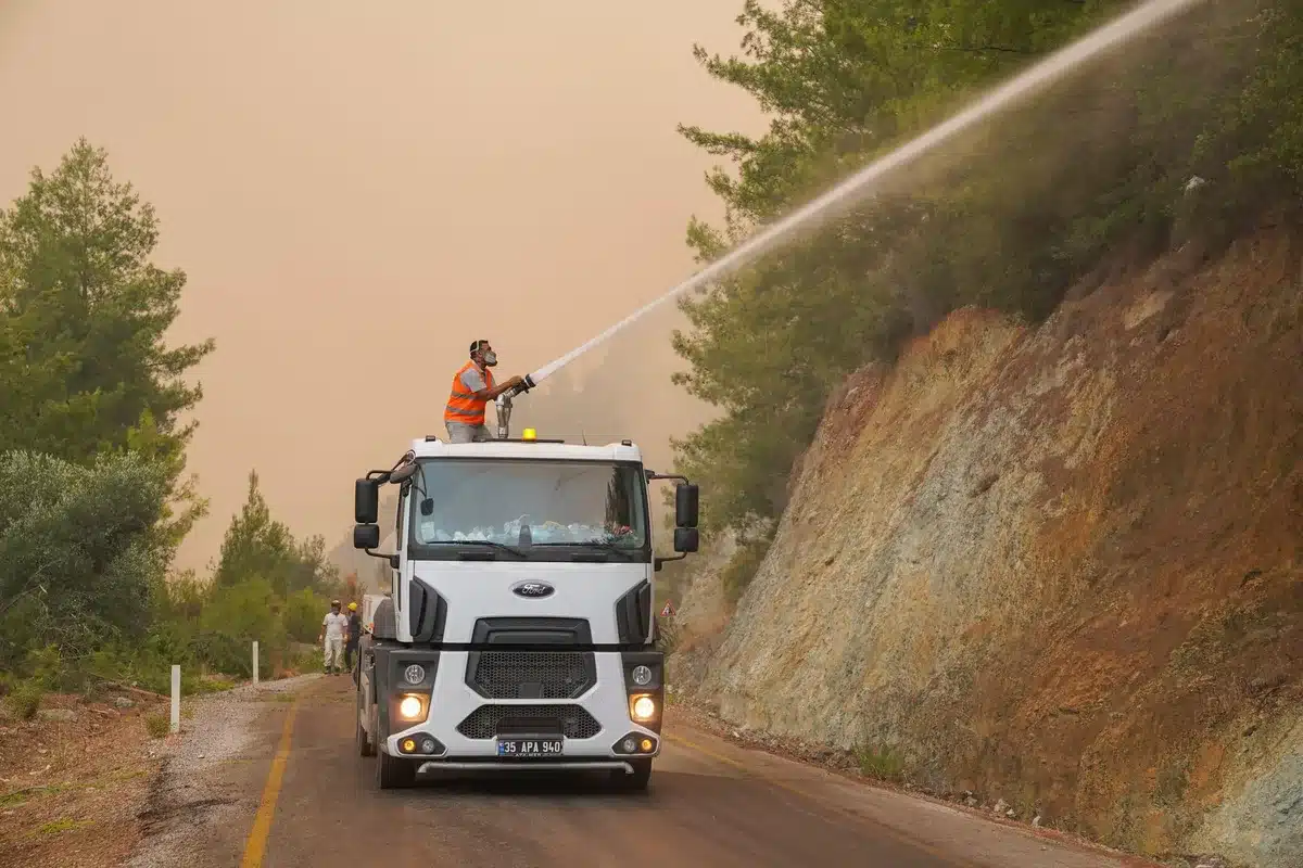 Vigili del fuoco con cannoni ad acqua aerei combattono un incendio boschivo su un pendio con fiamme e fumo denso