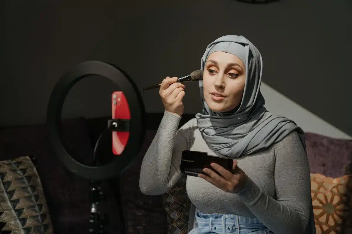 Persona che segue un tutorial di trucco su uno smartphone, con prodotti cosmetici sulla scrivania