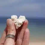 Mano con manicure ombré sfumata in toni pesca-corallo su asciugamano da spiaggia al tramonto