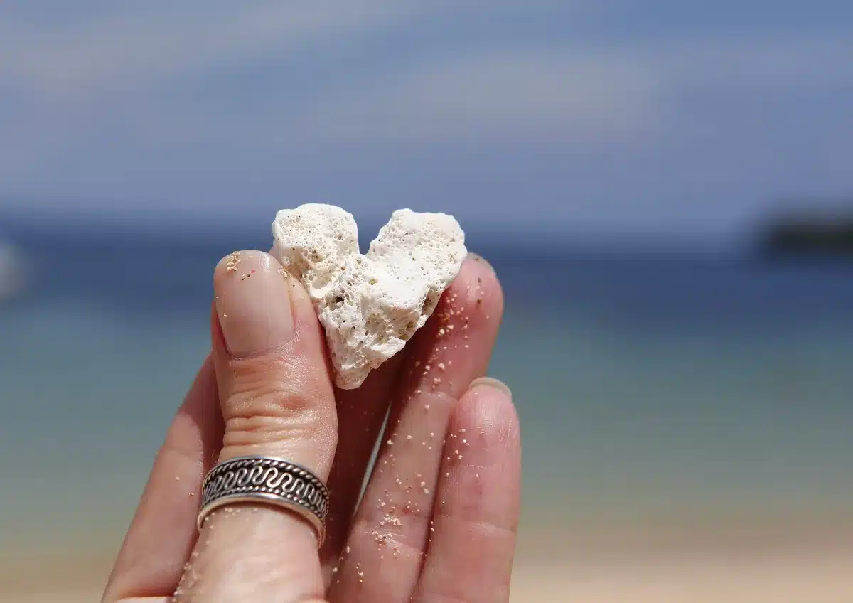 Mano con manicure ombré sfumata in toni pesca-corallo su asciugamano da spiaggia al tramonto
