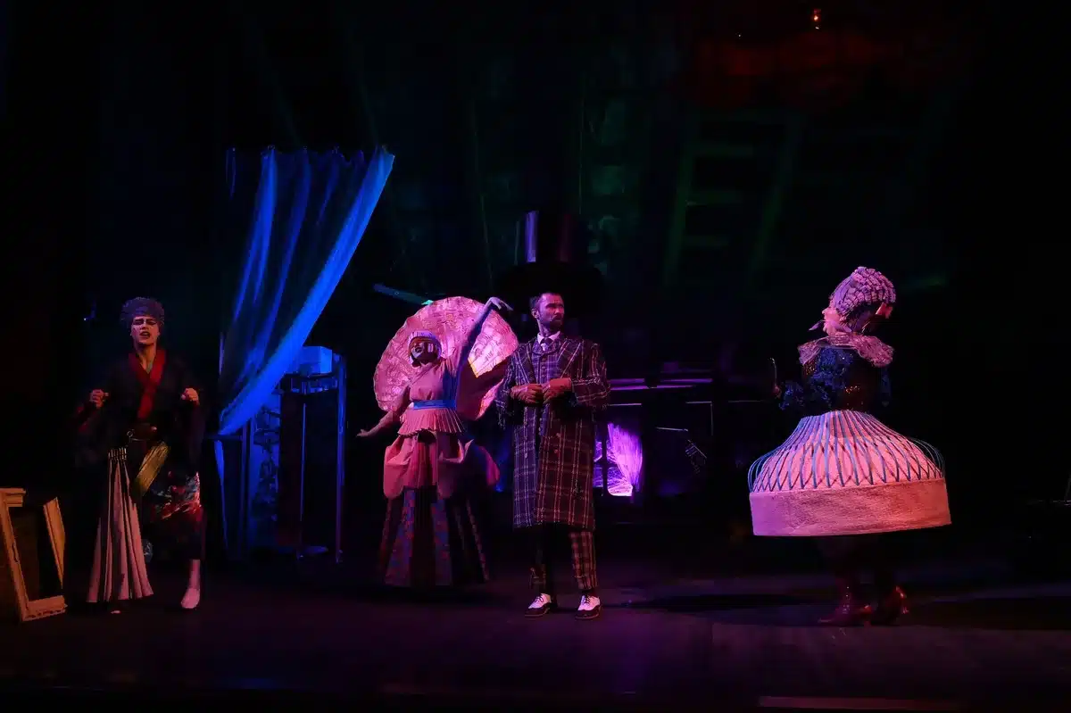 Scena teatrale con performer illuminati su palco durante una rappresentazione