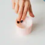 Persona che applica crema idratante al viso con le mani, circondata da prodotti skincare