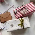 Mani che avvolgono regali colorati con nastri e carta durante le festivitร natalizie