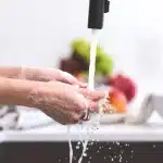 Mani che si lavano con una saponetta artigianale sotto acqua tiepida in un bagno minimalista.