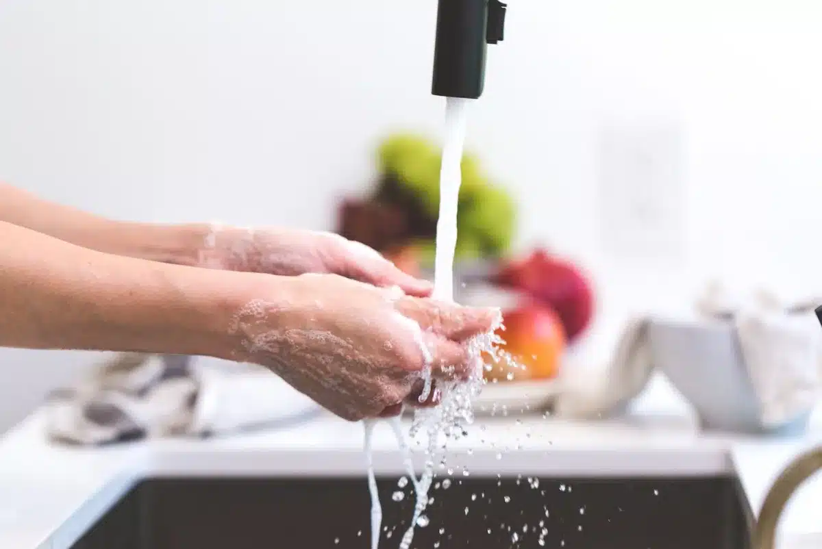 Mani che si lavano con una saponetta artigianale sotto acqua tiepida in un bagno minimalista.