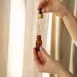 Goccia di siero di retinolo su un dito con prodotti skincare sfocati sullo sfondo