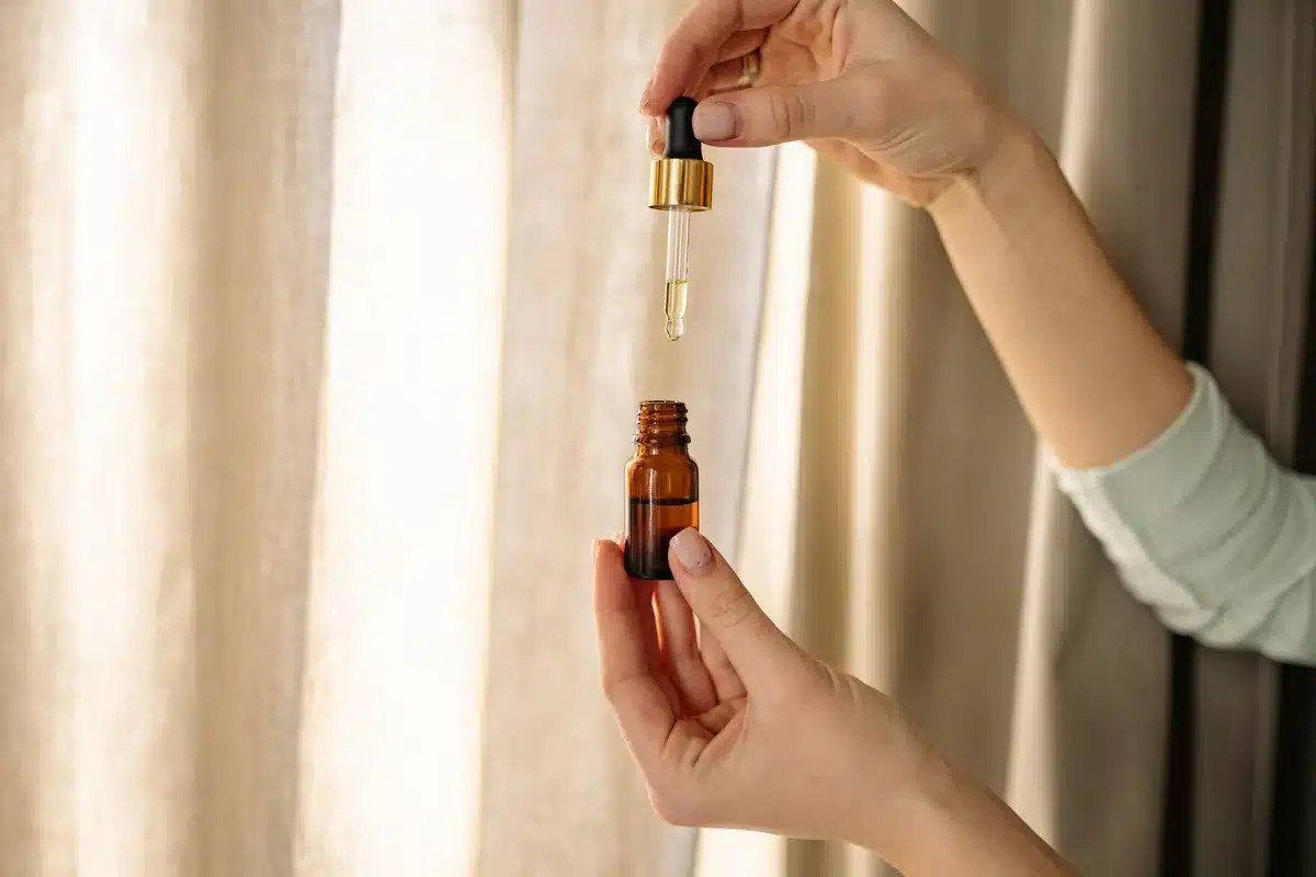 Goccia di siero di retinolo su un dito con prodotti skincare sfocati sullo sfondo