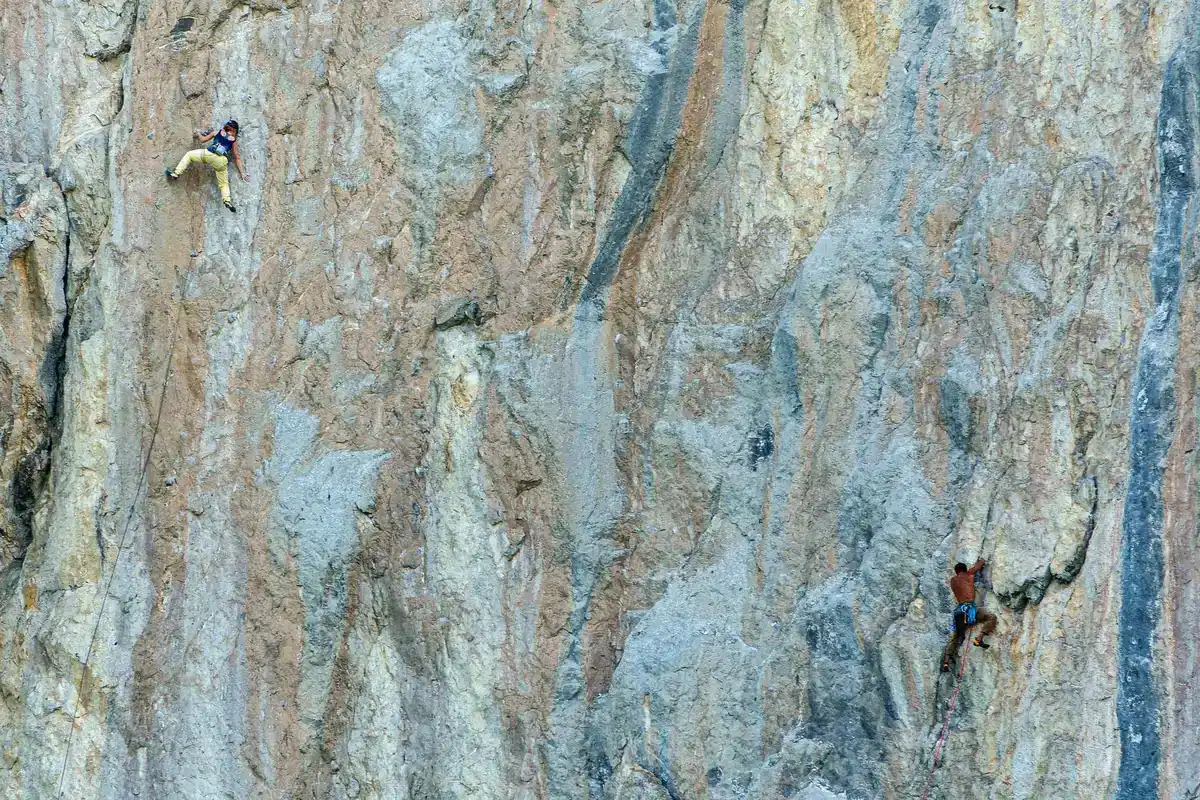 Arrampicatore su parete rocciosa esposta con corda e imbrago