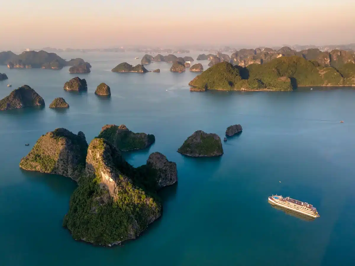 Isolotti calcarei della baia di Ha Long che emergono dal mare con barche tradizionali al tramonto