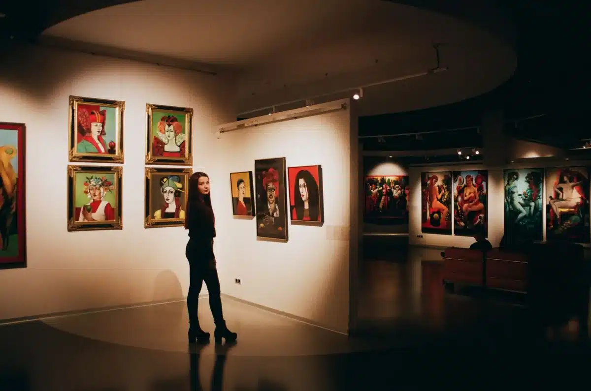 Sala di museo con dipinti esposti alle pareti e visitatori che osservano le opere