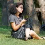 Persona di spalle osserva lo schermo di uno smartphone illuminato da immagini ritoccate, circondata da prodotti cosmetic