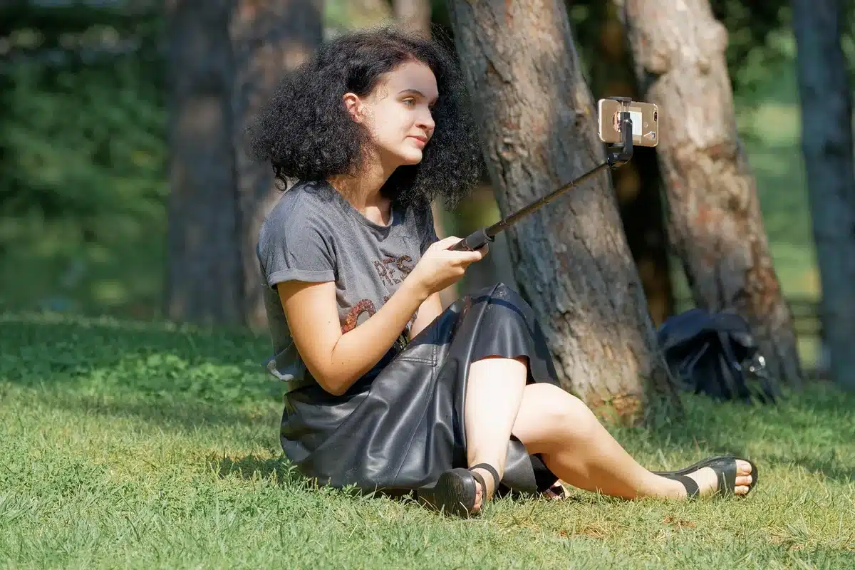Persona di spalle osserva lo schermo di uno smartphone illuminato da immagini ritoccate, circondata da prodotti cosmetic