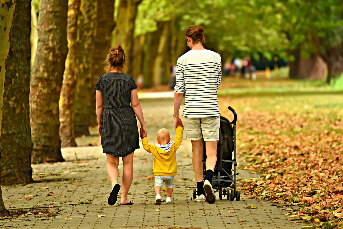 Gruppo di persone che camminano insieme in un parco con alberi, una persona fa stretching