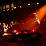 Due figure anonime sul palco di un concerto con pubblico sfocato e luci