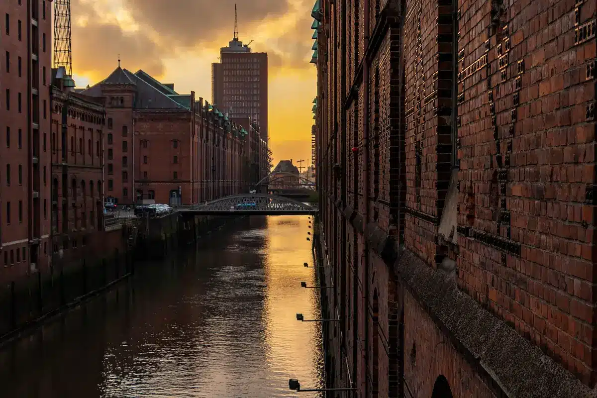 Passanti camminano lungo il Naviglio di Milano, tra edifici storici e l'arco di Porta Ticinese al tramonto