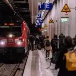 Passeggeri in attesa su un binario ferroviario con tabellone partenze bloccato
