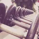Angolo palestra con manubri, bande elastiche e asciugamano su una panca, mano anonima che prende un peso
