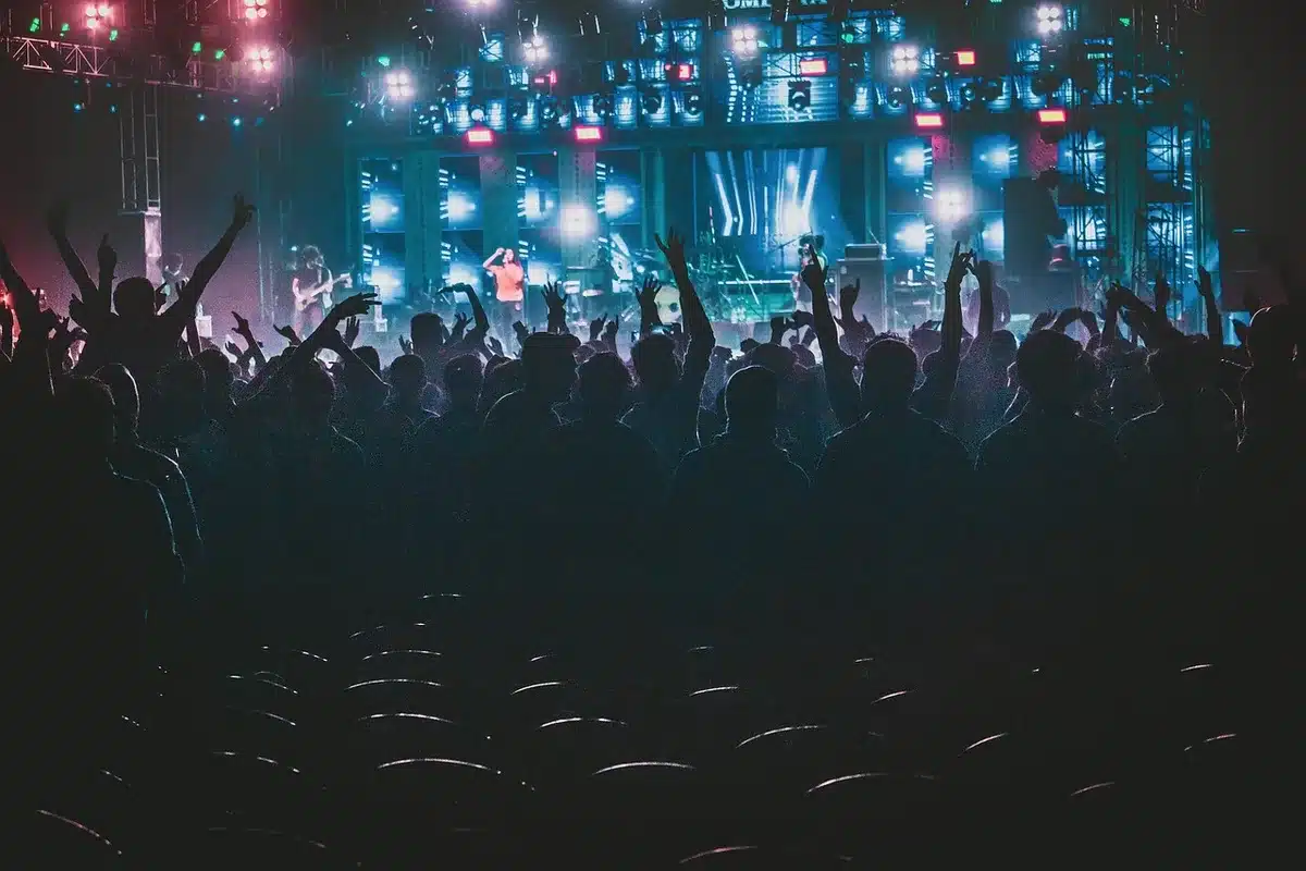 Pubblico anonimo in platea e palco con luci calde ed elementi scenici astratti