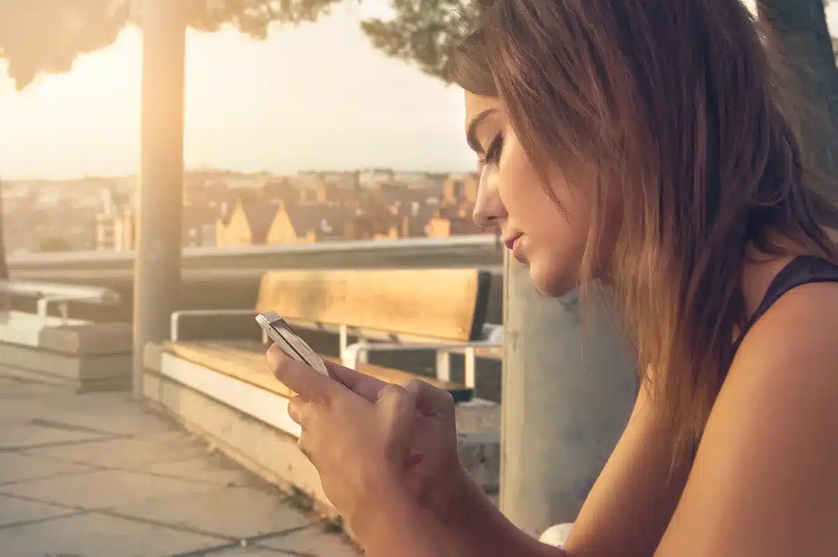 Donna in controluce seduta con smartphone spento su un tavolo in uno spazio espositivo