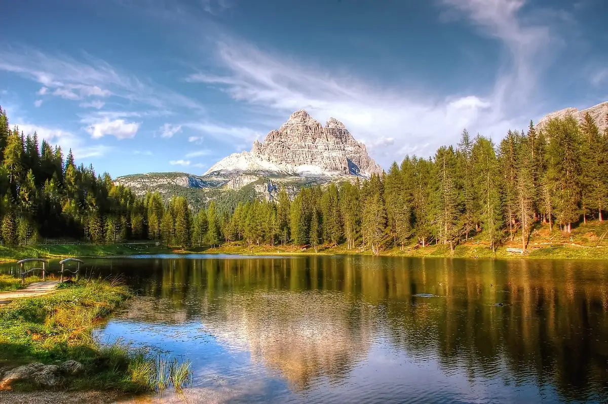 Lago alpino calmo con riflesso delle montagne e passerella panoramica