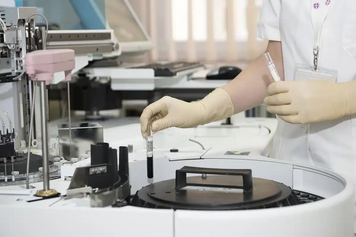 Vetreria di laboratorio e flacone cosmetico sfocato su bancone, mani con guanti