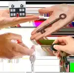 Mani anonime che usano un'app di gestione affitti con chiavi e documenti su tavolo